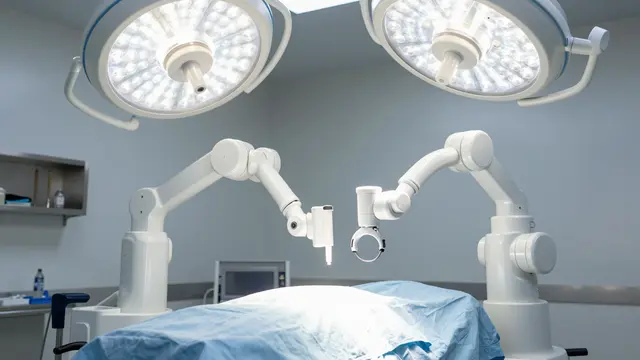White surgical robot arms are positioned over a draped operating table under overhead surgical lights