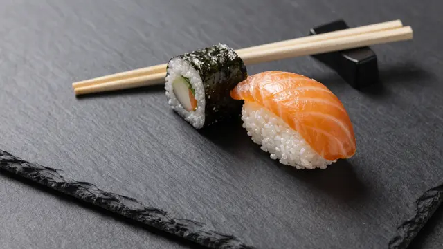 Two pieces of sushi and wooden chopsticks sit at the top edge of a dark slate background with empty copy space.