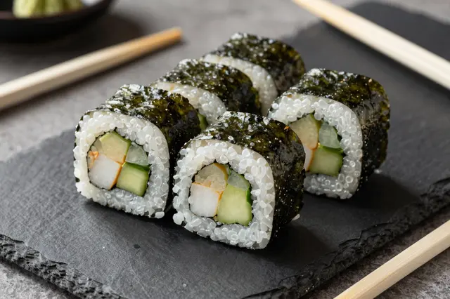 Vegetable maki sushi rolls arranged on a dark slate serving platter with wooden chopsticks in the background.