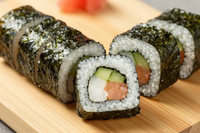 Close-up of sliced maki sushi rolls arranged neatly on a light wooden cutting board
