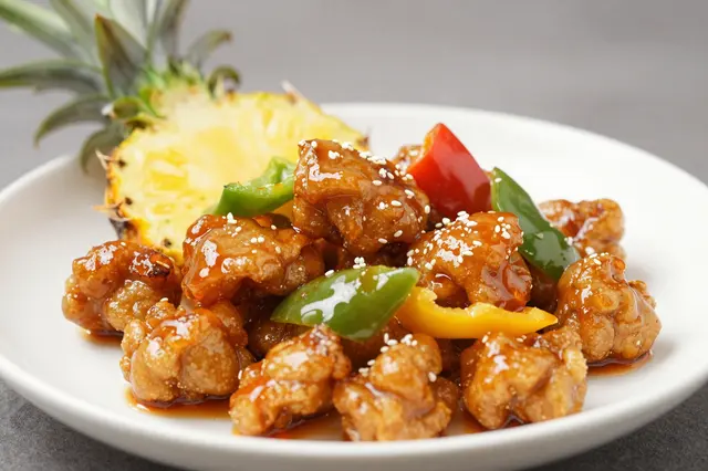 Glazed sweet and sour pork with peppers, pineapple and sesame seeds on a white plate