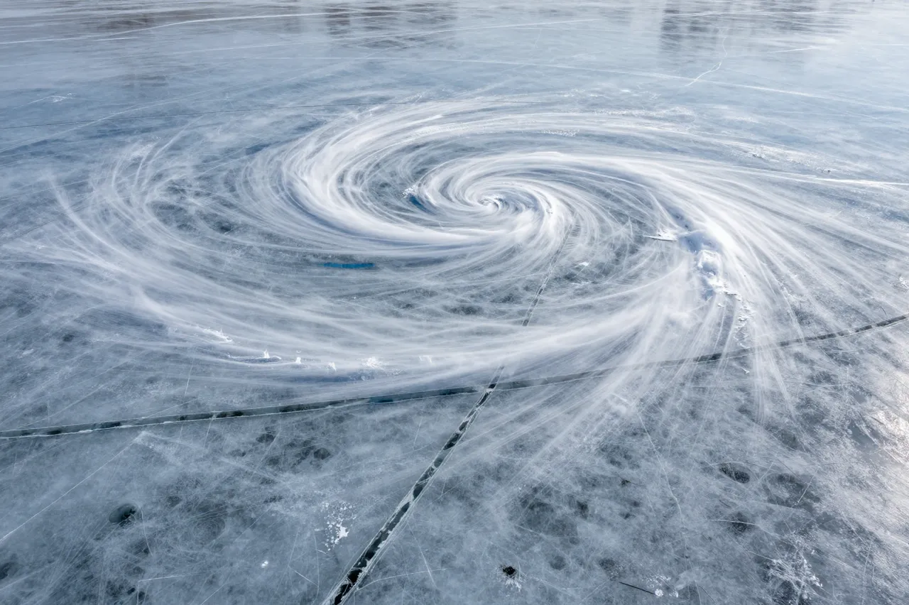 Aerial view of a spiral swirling snow and crack pattern across the surface of a frozen lake