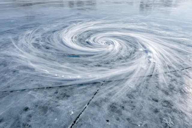 Aerial view of a spiral swirling snow and crack pattern across the surface of a frozen lake