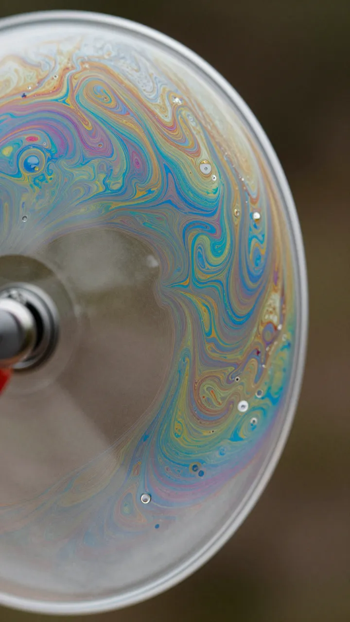 Macro close-up of a soap film in a wire loop showing intricate iridescent swirling patterns