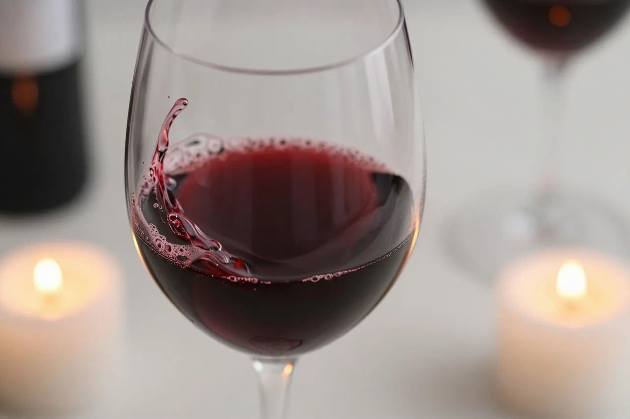 A close up of red wine swirling in a wine glass flanked by lit tealight candles on a table