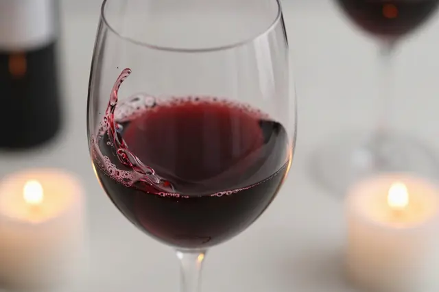 A close up of red wine swirling in a wine glass flanked by lit tealight candles on a table