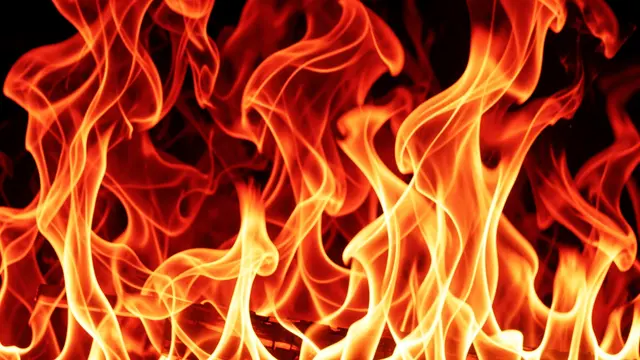 Bright swirling red and yellow fire flames twist against a dark black background