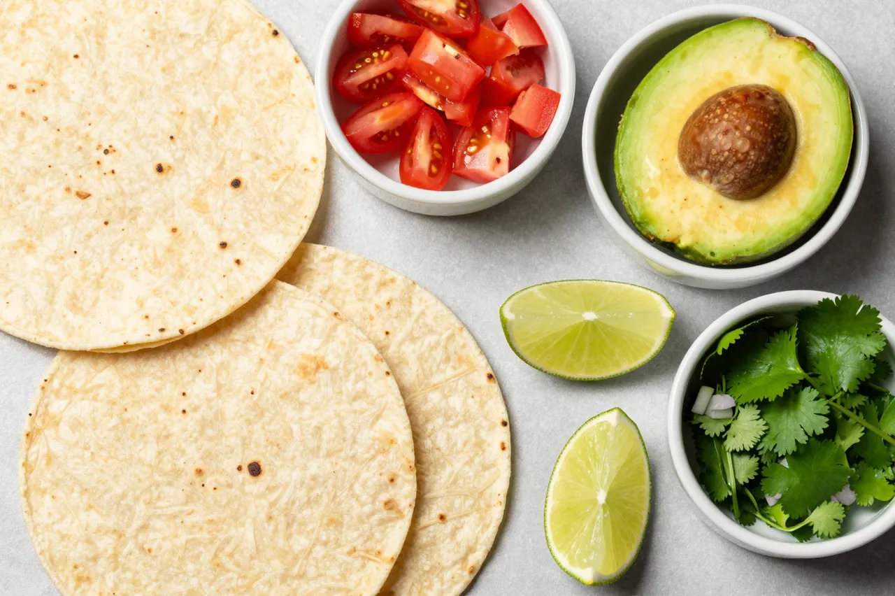 Top-down flat lay of corn tortillas and fresh taco toppings arranged in small bowls on a light gray countertop