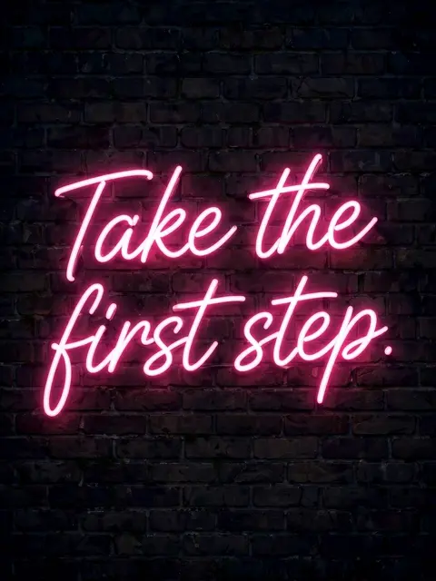 Glowing pink neon sign reading "Take the first step." mounted on a dark nighttime brick wall