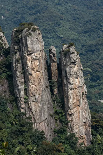 Tall weathered rock spires rise steeply from a dense forested mountain slope