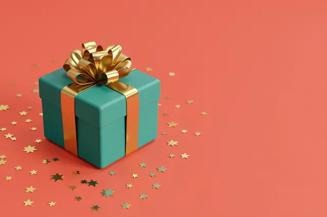 A teal gift box with a gold bow sits with star confetti against a solid coral background with empty right copy space