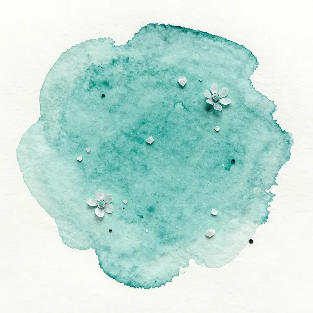 A top view of a teal watercolor wash with salt crystal blooms scattered across textured white paper