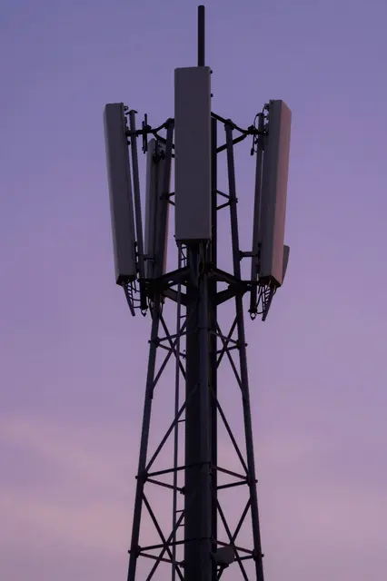Top section of a cellular telecom mast silhouetted against a soft purple gradient dusk sky