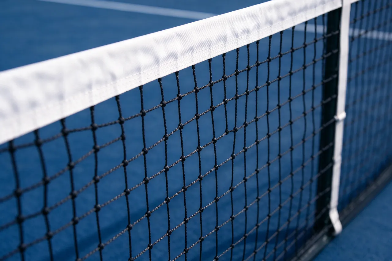 Close-up of a tennis net's white top tape with a blurred blue hard tennis court in the background