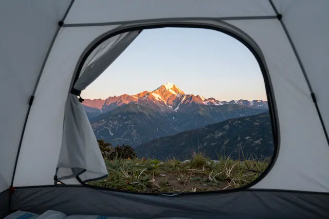 View from inside an open tent looking out at sunlit snow-capped mountains at dawn