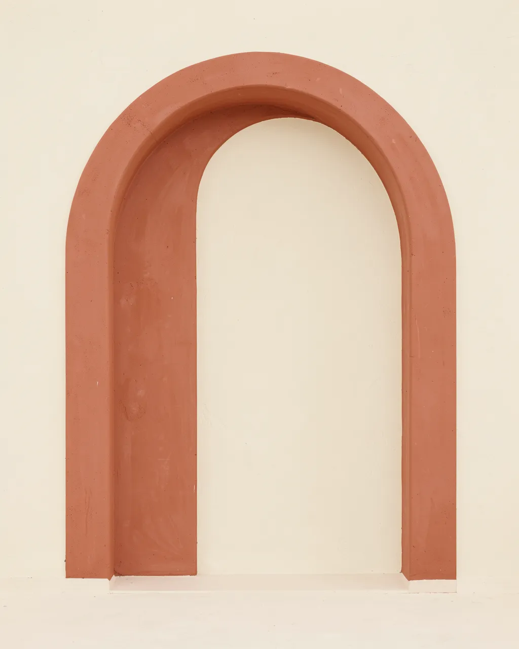 Smooth terracotta arched niche set against a plain pale cream plaster wall