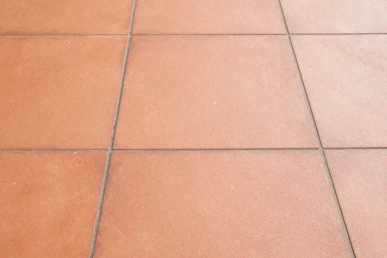 A close-up view of square terracotta floor tiles with gray grout lines forming a neat grid pattern.