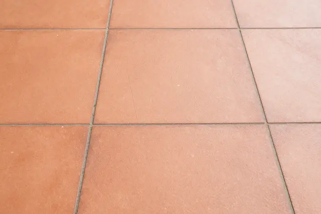 A close-up view of square terracotta floor tiles with gray grout lines forming a neat grid pattern.