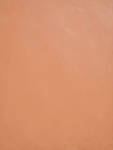 Full frame view of matte hand-smoothed terracotta clay plaster surface with even flat lighting
