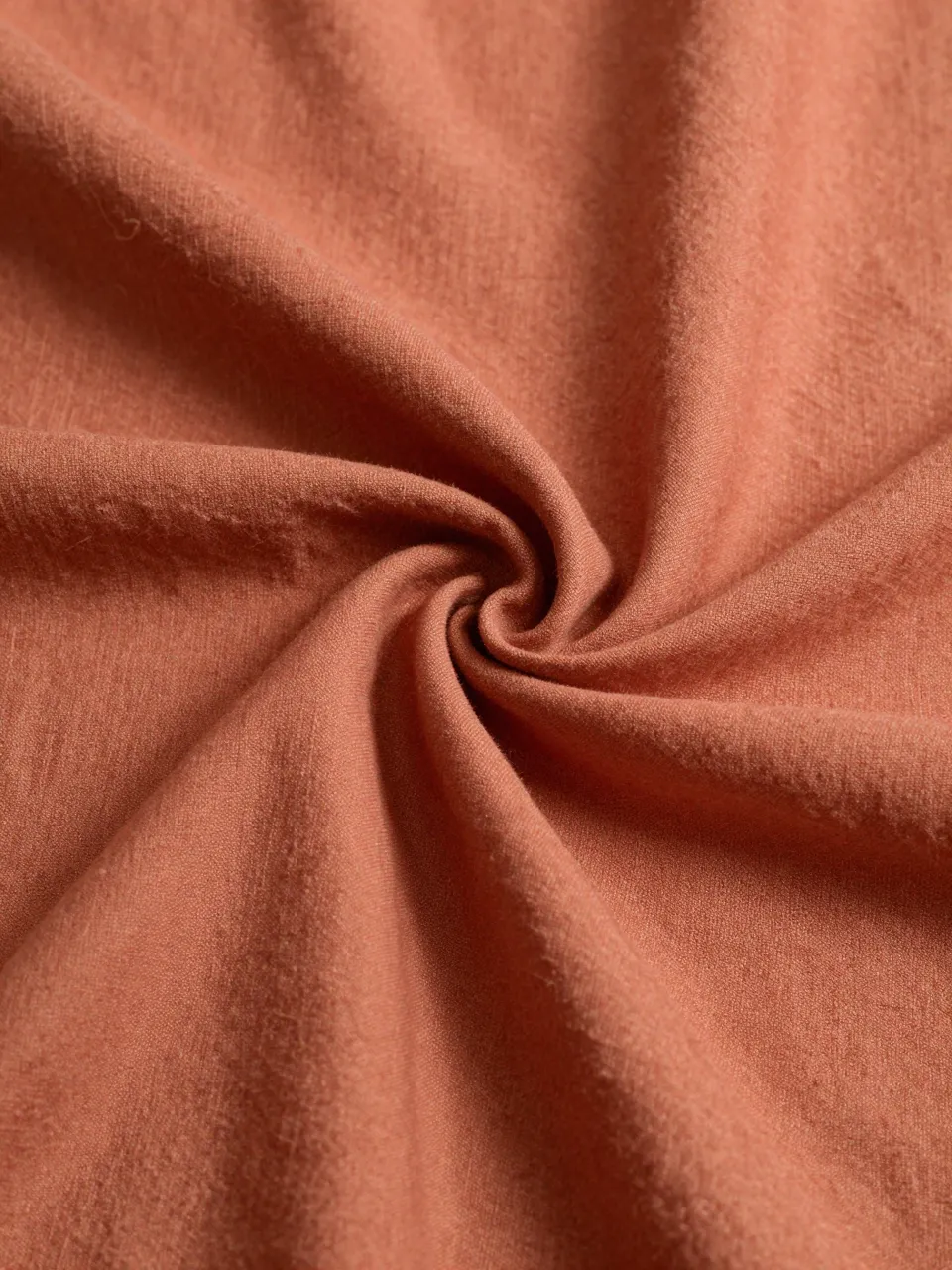 Close up of twisted soft terracotta linen fabric with warm side lighting highlighting its texture