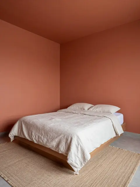 A serene minimalist bedroom with terracotta walls, low linen bed, and woven jute rug.