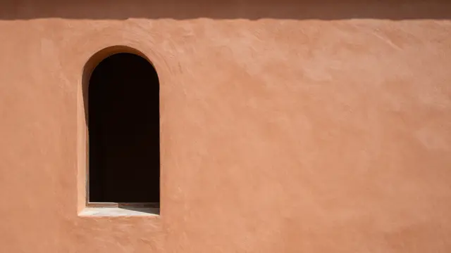 Textured warm terracotta plaster wall featuring a narrow dark arched window on the left side