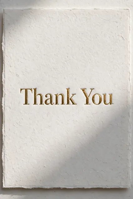 Embossed gold foil 'Thank You' lettering rests on textured thick white deckled cardstock with soft raking daylight.