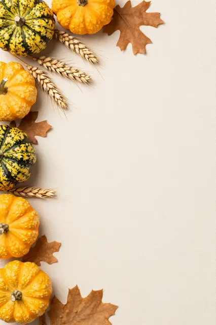 Autumn gourds, wheat stalks, and oak leaves line the left edge of a cream linen background with empty copy space.