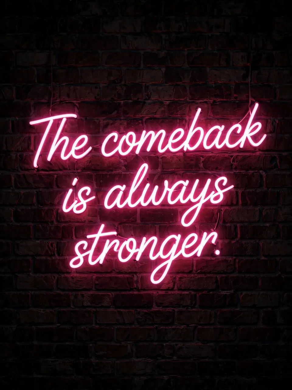 Pink neon script sign reading "The comeback is always stronger." glows on a dark brick wall at night