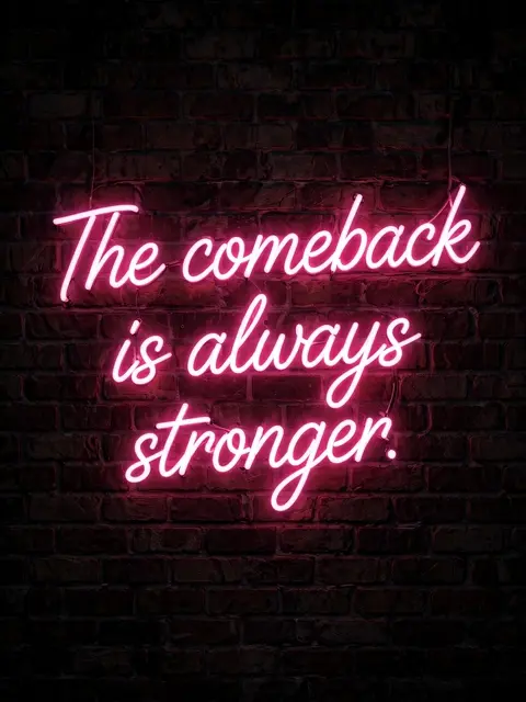 Pink neon script sign reading "The comeback is always stronger." glows on a dark brick wall at night