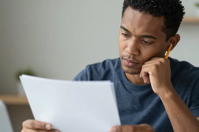 A mixed-race man in his thirties holds blank paper, resting his chin on his hand with a pencil behind his ear.