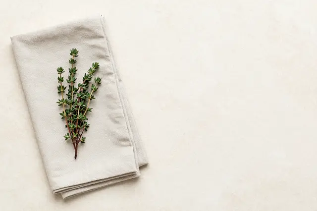 Fresh thyme sprigs rest on a folded linen napkin at the left of a pale stone countertop with empty copy space to the right
