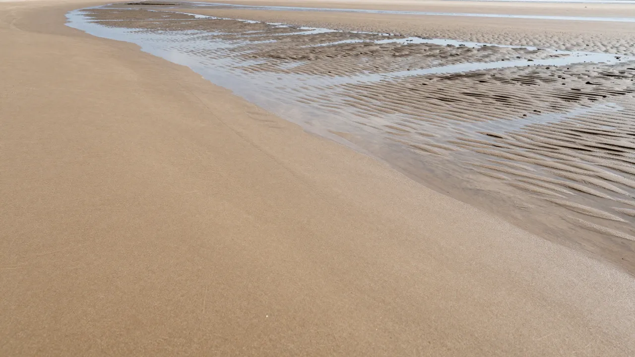 Wide empty low-tide beach showing smooth dry sand, rippled wet sand and shallow tidal pools