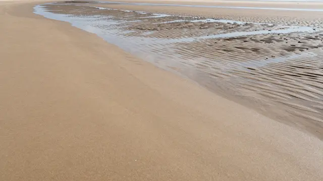 Wide empty low-tide beach showing smooth dry sand, rippled wet sand and shallow tidal pools