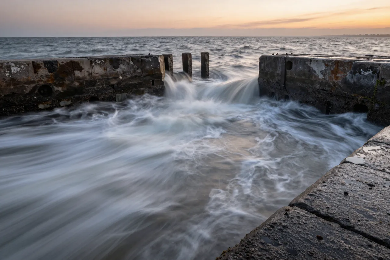 Long exposure shot of incoming swirling tide moving through an old stone slipway during warm sunset