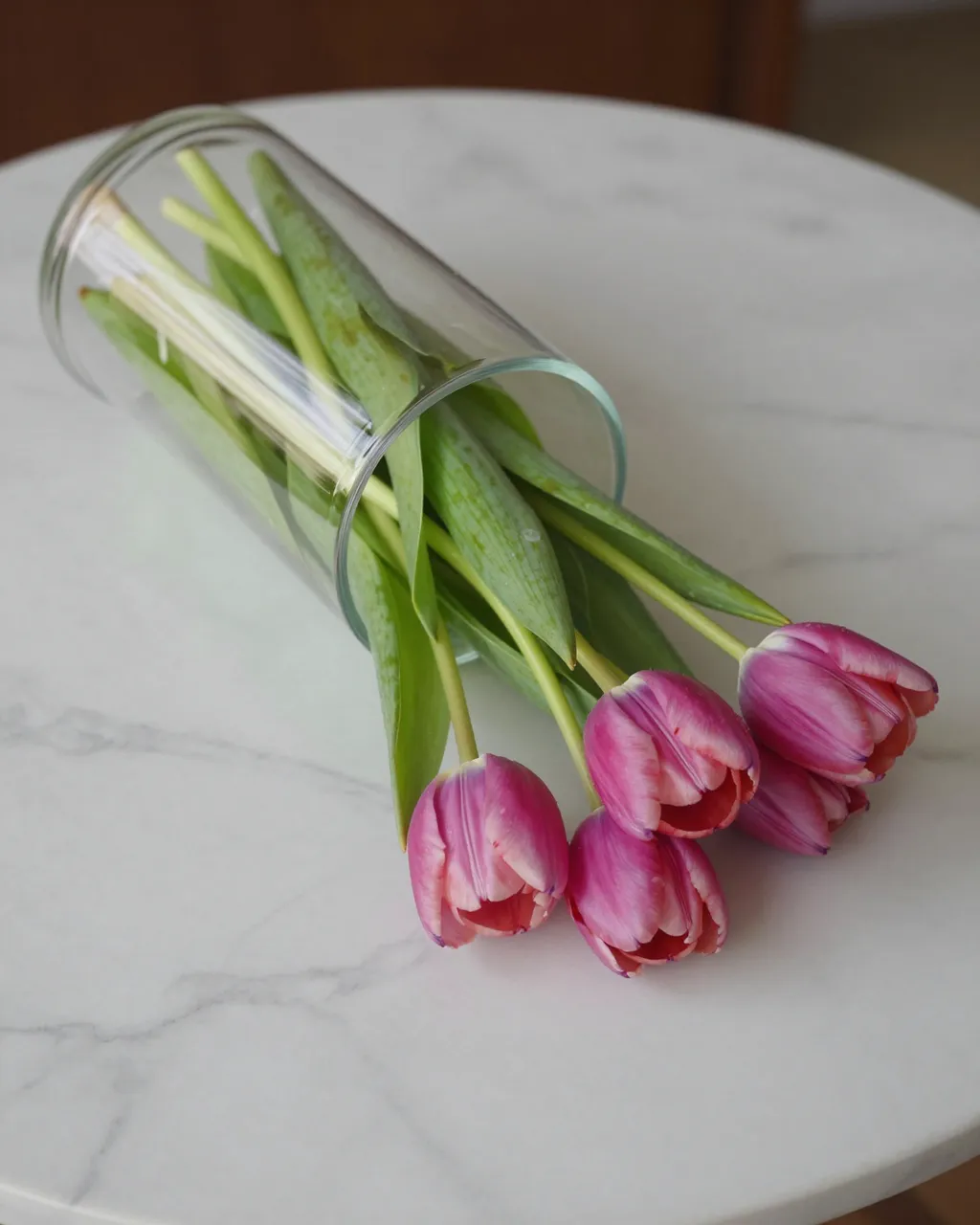 Pink tulips spilling from a fallen glass vase resting on a white marble table
