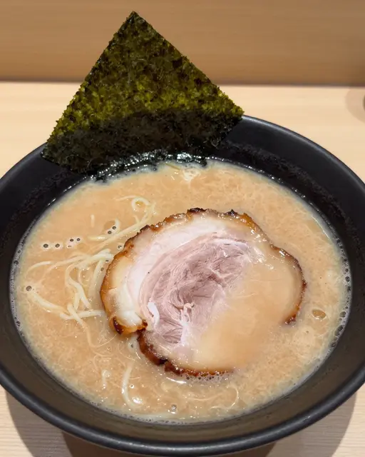 A bowl of creamy tonkotsu ramen with chashu pork and nori served on a light wooden table