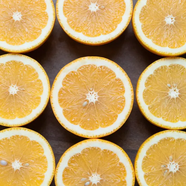 Neatly arranged cross-section orange halves viewed from above on a dark matte surface