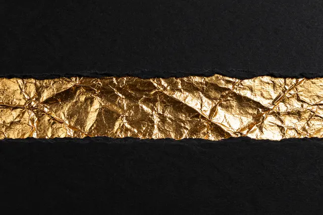 Torn matte black paper reveals a horizontal strip of crinkled reflective gold foil across the frame