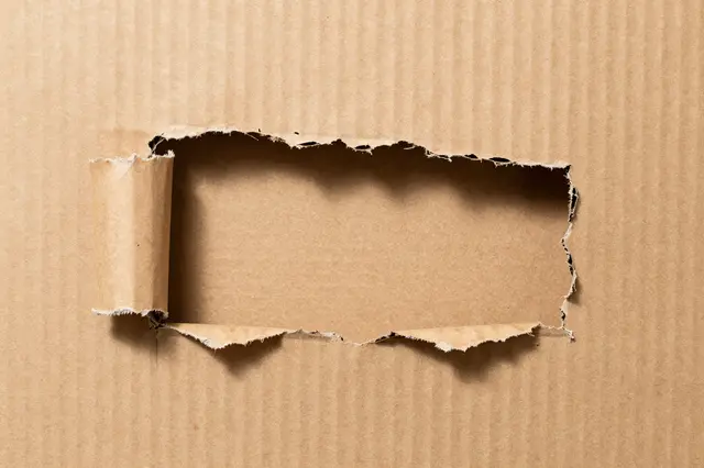 Close-up of torn brown corrugated cardboard with a ragged rectangular opening and curled left edge
