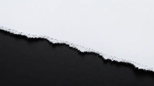 A close-up of a rough, frayed torn white paper edge resting above a solid black background