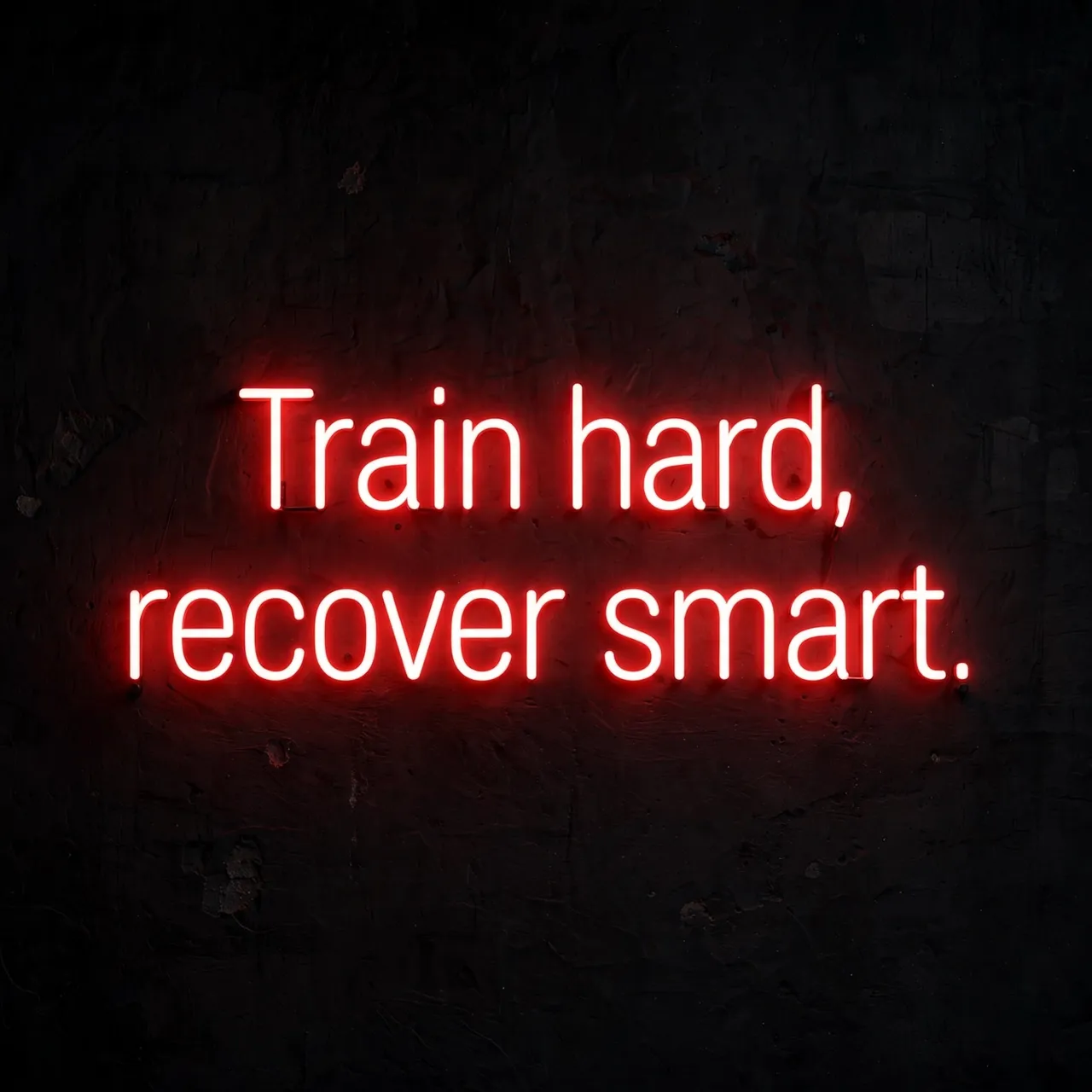 Glowing red neon sign reading "Train hard, recover smart." mounted on a dark textured gym wall