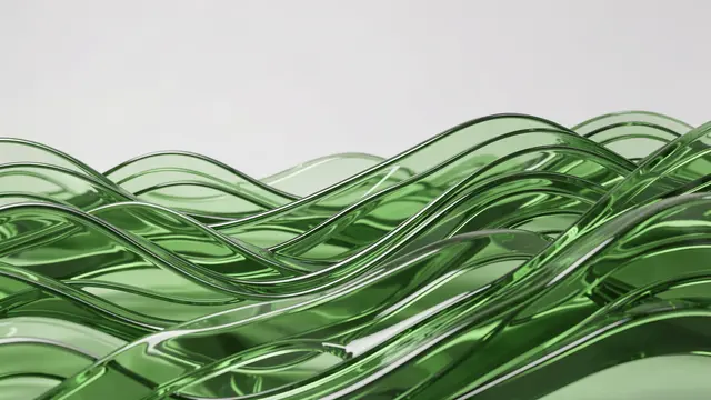 Stacked rolling translucent green glass waves sit against a pale neutral background under soft studio lighting
