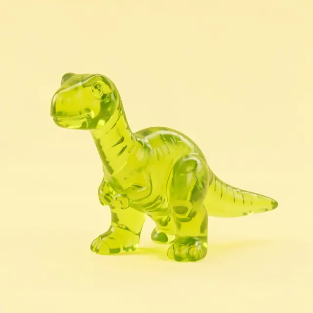 A translucent lime green gummy-style 3D rendered dinosaur sits on a pale yellow solid background