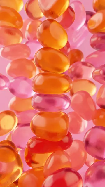 Close-up of stacked glossy translucent orange and pink gummy blobs against a solid pink background
