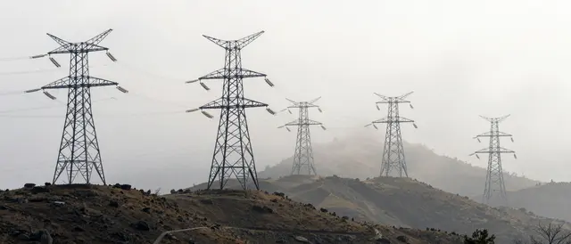 A line of electricity transmission towers stands in a receding row across rocky fog-shrouded hills