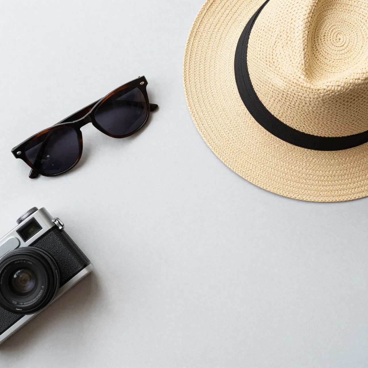 Top view of a straw hat, sunglasses and vintage camera arranged on a pale gray flat surface.