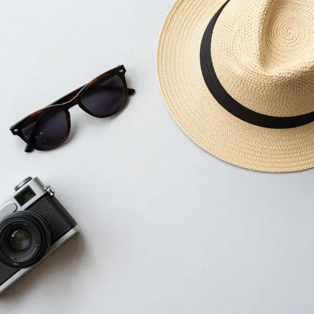 Top view of a straw hat, sunglasses and vintage camera arranged on a pale gray flat surface.