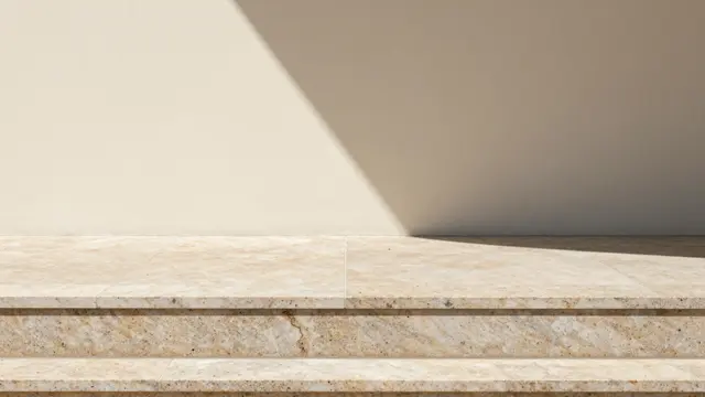 Wide travertine product plinth sits below a cream wall lit by sharp angled sunlight