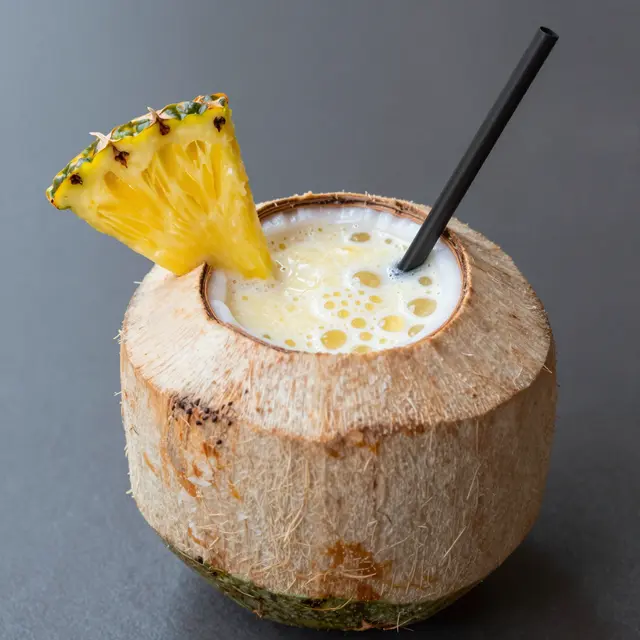 Creamy tropical smoothie served in a hollowed coconut with a pineapple wedge garnish and black straw